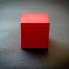 Bright red cube resting on a dark surface, showcasing vibrant contrast.
